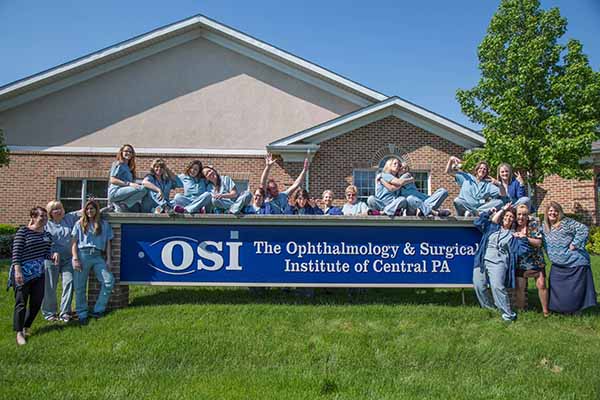 The staff at OSI gather around the outside sign and pose for a photo.
