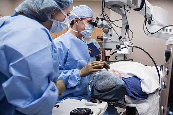 Doctor looking through medical equipment while he and the nurse perform a medical procedure on the patient’s eye.