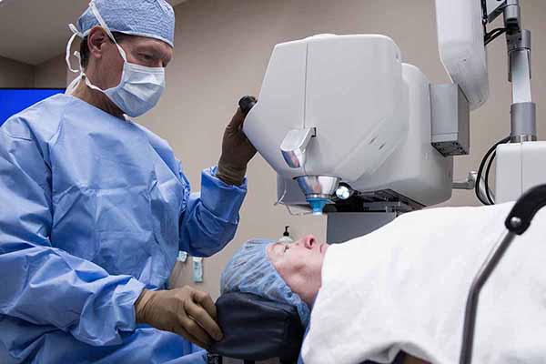 Doctor assisting patient under laser machine for medical eye procedure.