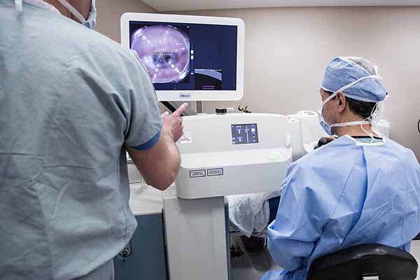 Doctor and nurse looking at the medical equipment that is displaying a close-up view of the patient’s eye.